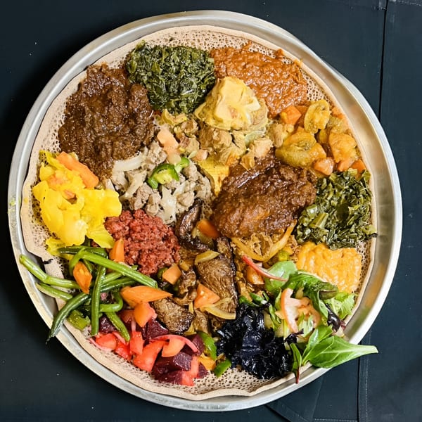 A large platter of Axum Ethiopian food with various colorful stews, vegetables, and meats on injera bread.