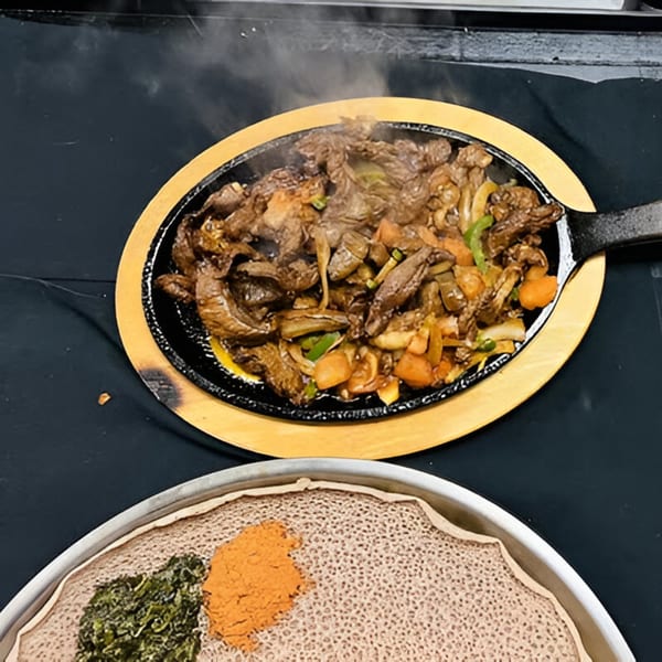Sizzling Ethiopian tibs with vegetables in a hot skillet, alongside injera bread with two colorful toppings.