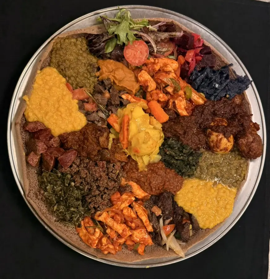 Ethiopian Chef’s Combo platter featuring 11 vibrant vegetable dishes and an assortment of meat specialties including chicken, lamb, beef tibs, kitfo, gored gored, and zilzil tibs, all served on fresh gluteen free injera.